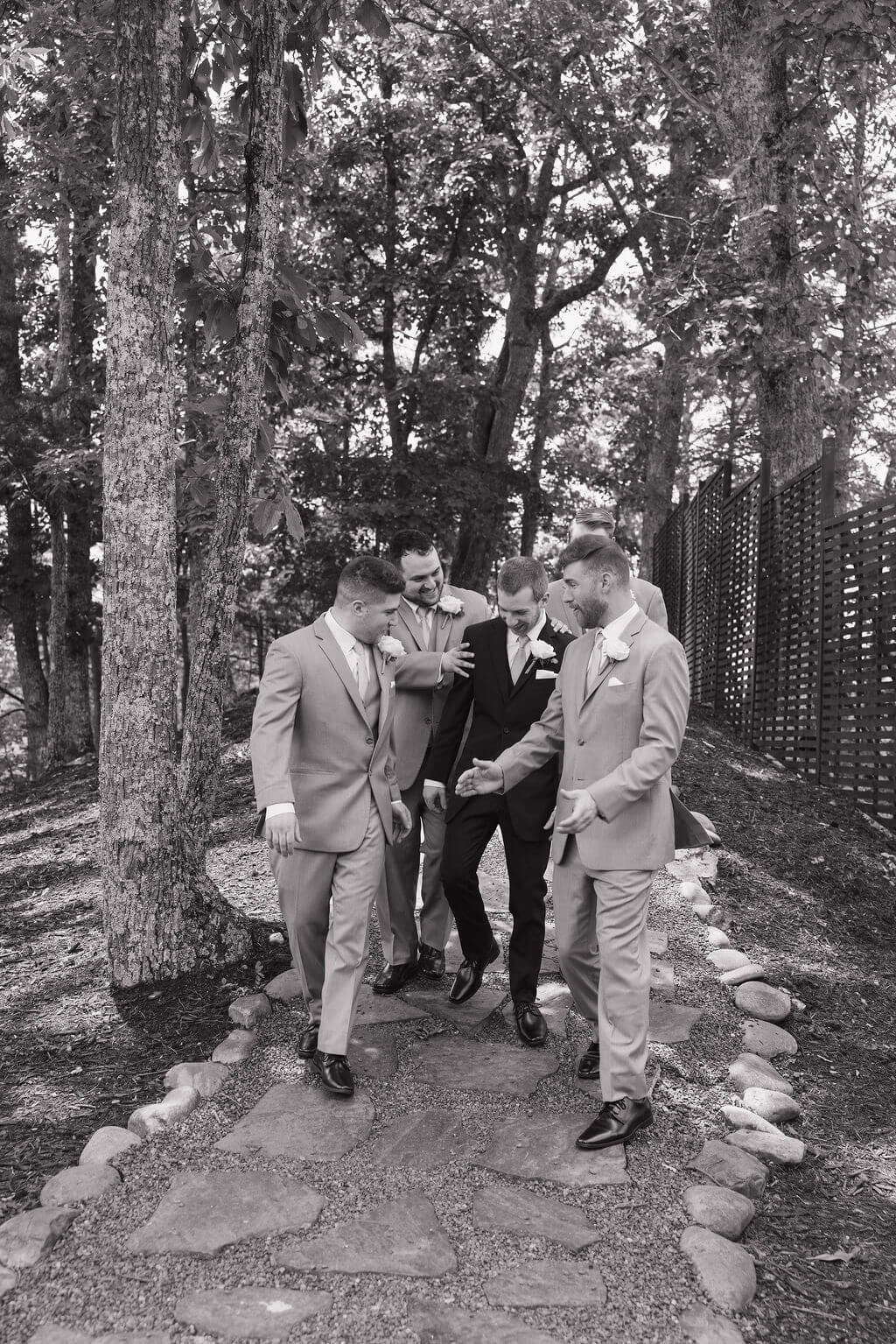 Black-and-white photo of the groom and groomsmen walking along a wooded stone pathway before the wedding.