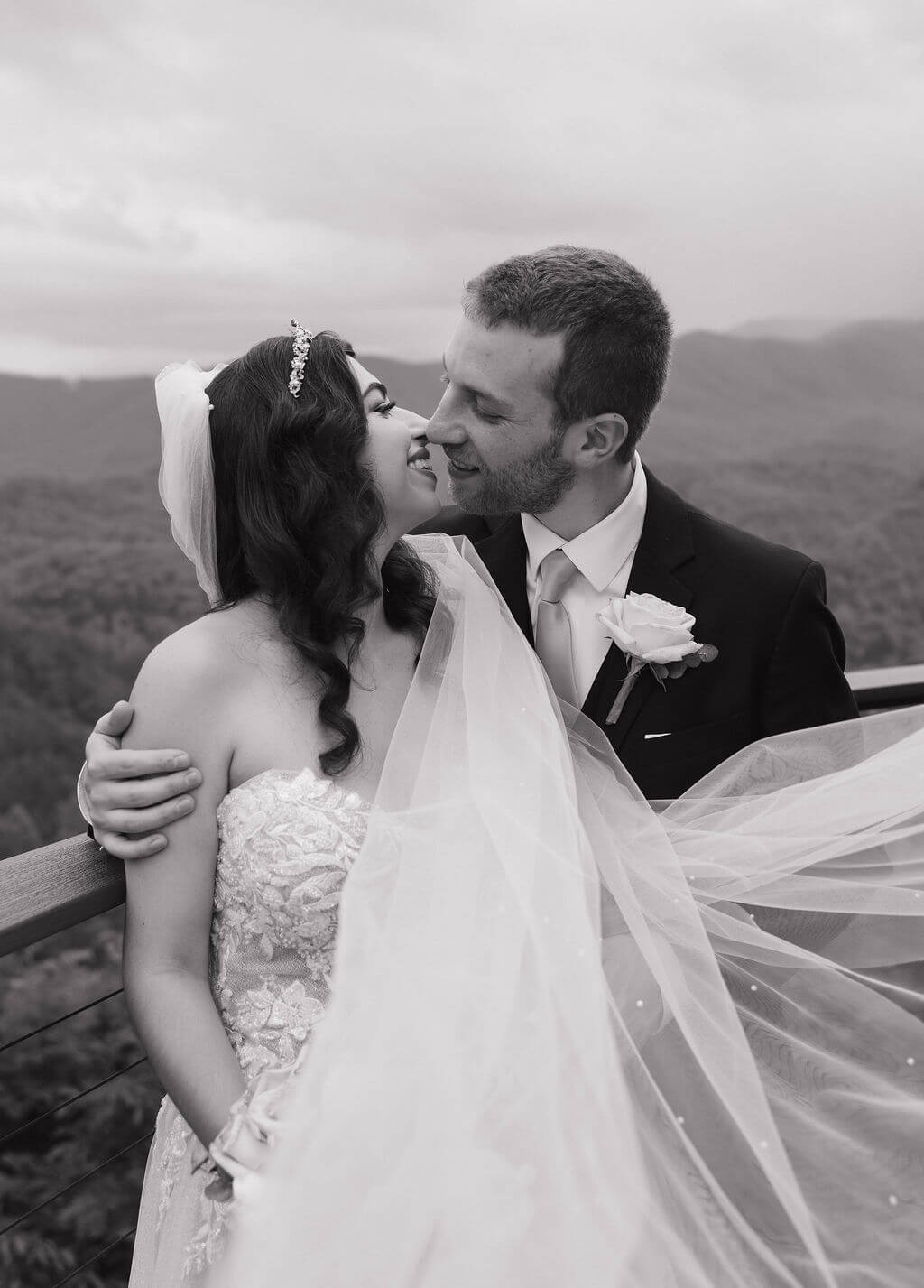 Black-and-white close-up of the bride and groom kissing with the bride’s veil blowing around them.