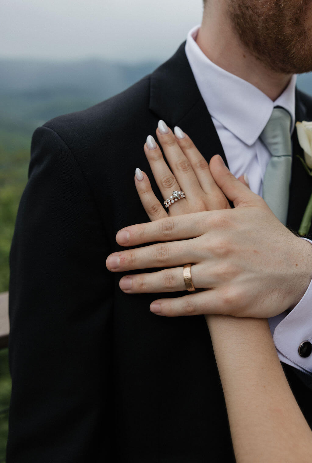 Close-up of the bride and groom showing their wedding rings against the groom’s black suit.