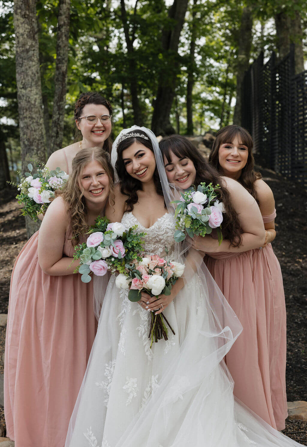 Bride smiling with her bridesmaids in blush dresses and holding pastel wedding bouquets.