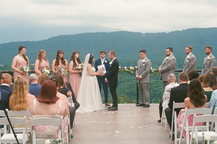 Bride and groom standing together during their outdoor wedding ceremony with guests and Smoky Mountain views surrounding them.