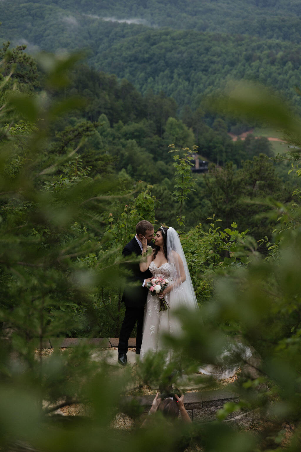Bride and groom standing together among the trees with layered Smoky Mountain views in the distance.
