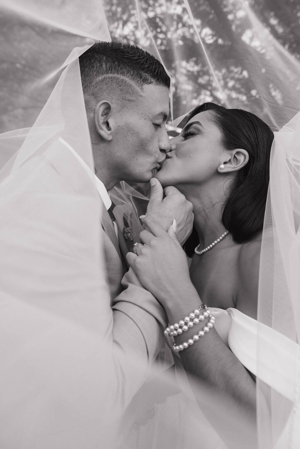Black-and-white close-up of the bride and groom kissing beneath her wedding veil.