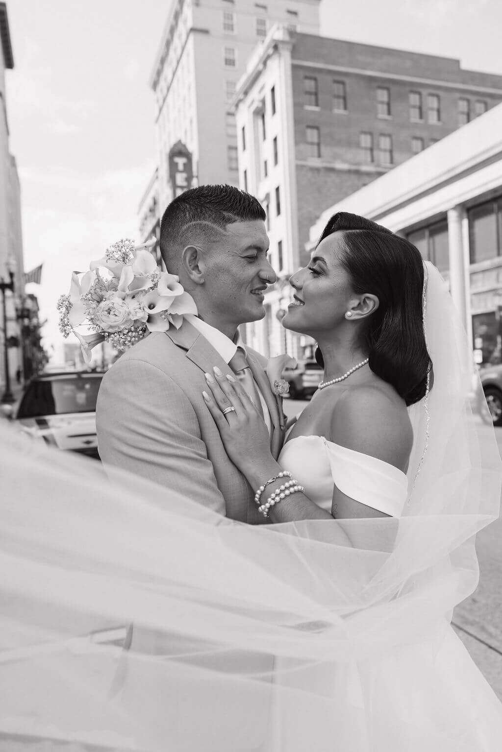 Black-and-white portrait of the bride and groom smiling at each other while wrapped in her veil on a downtown Knoxville street.
