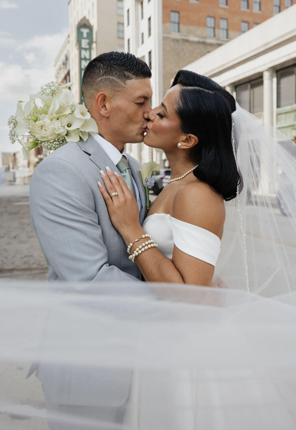 Bride and groom kissing beneath her veil with her white bouquet held between them in downtown Knoxville.