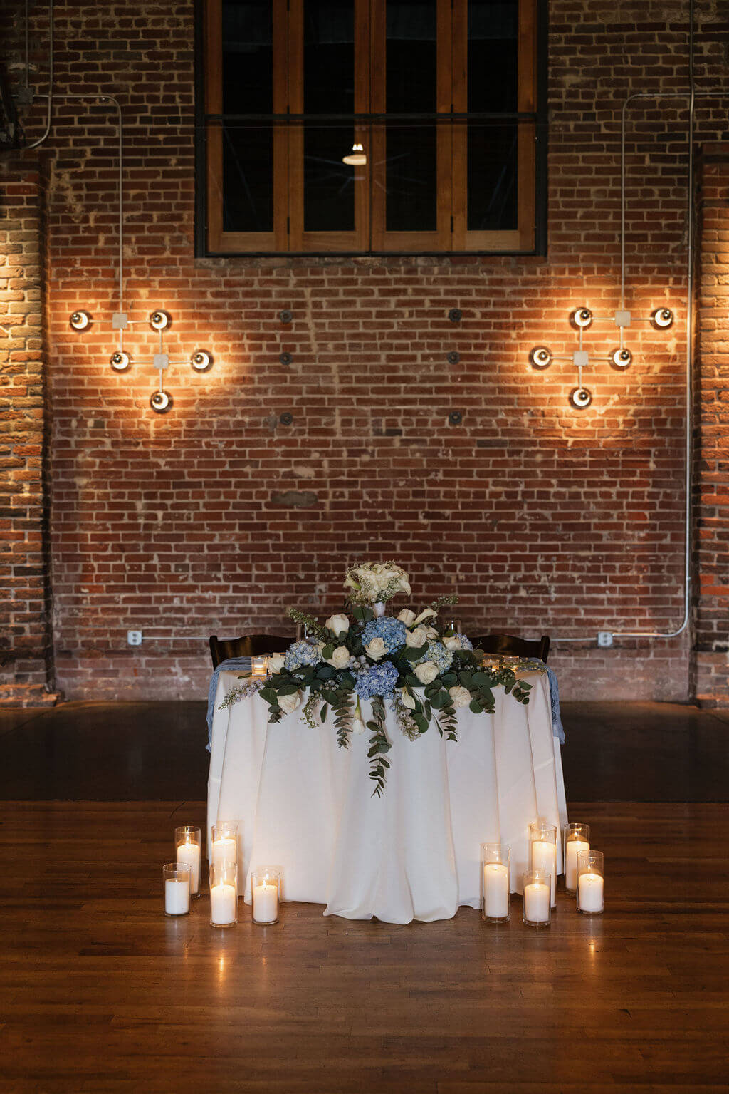 Sweetheart table decorated with white flowers and glowing candles against the exposed brick walls of The Mill and Mine.