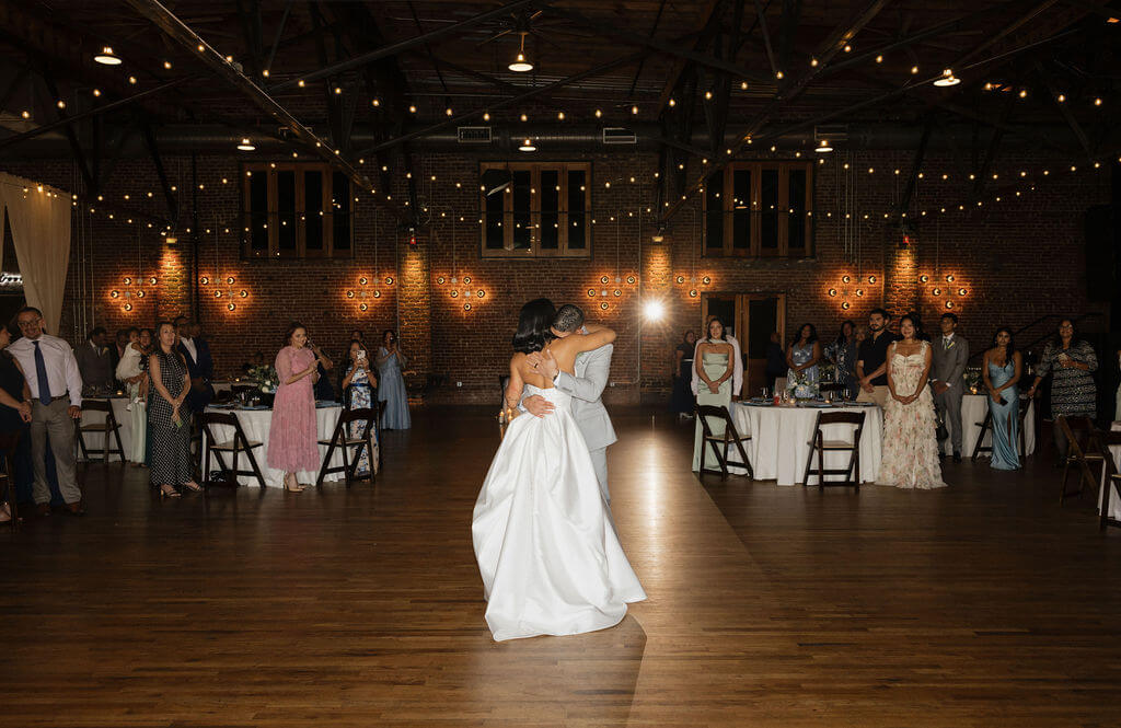 Bride and groom dancing in the center of The Mill and Mine reception space beneath string lights as guests watch.