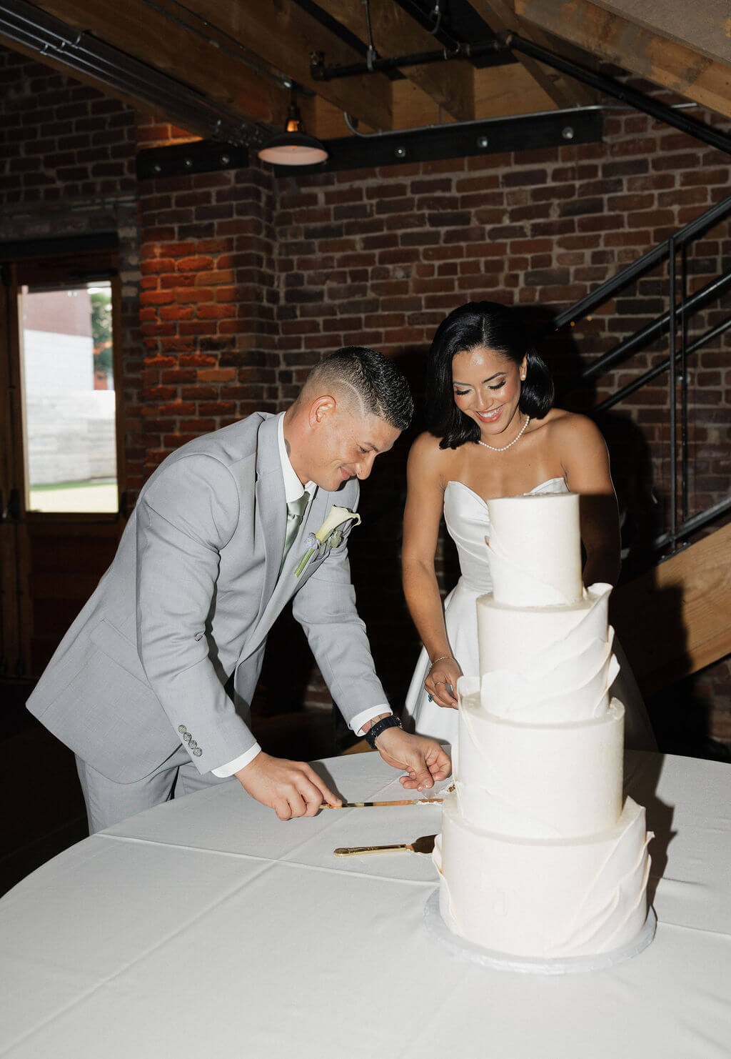 Bride and groom smiling together as they cut their white wedding cake at the reception.
