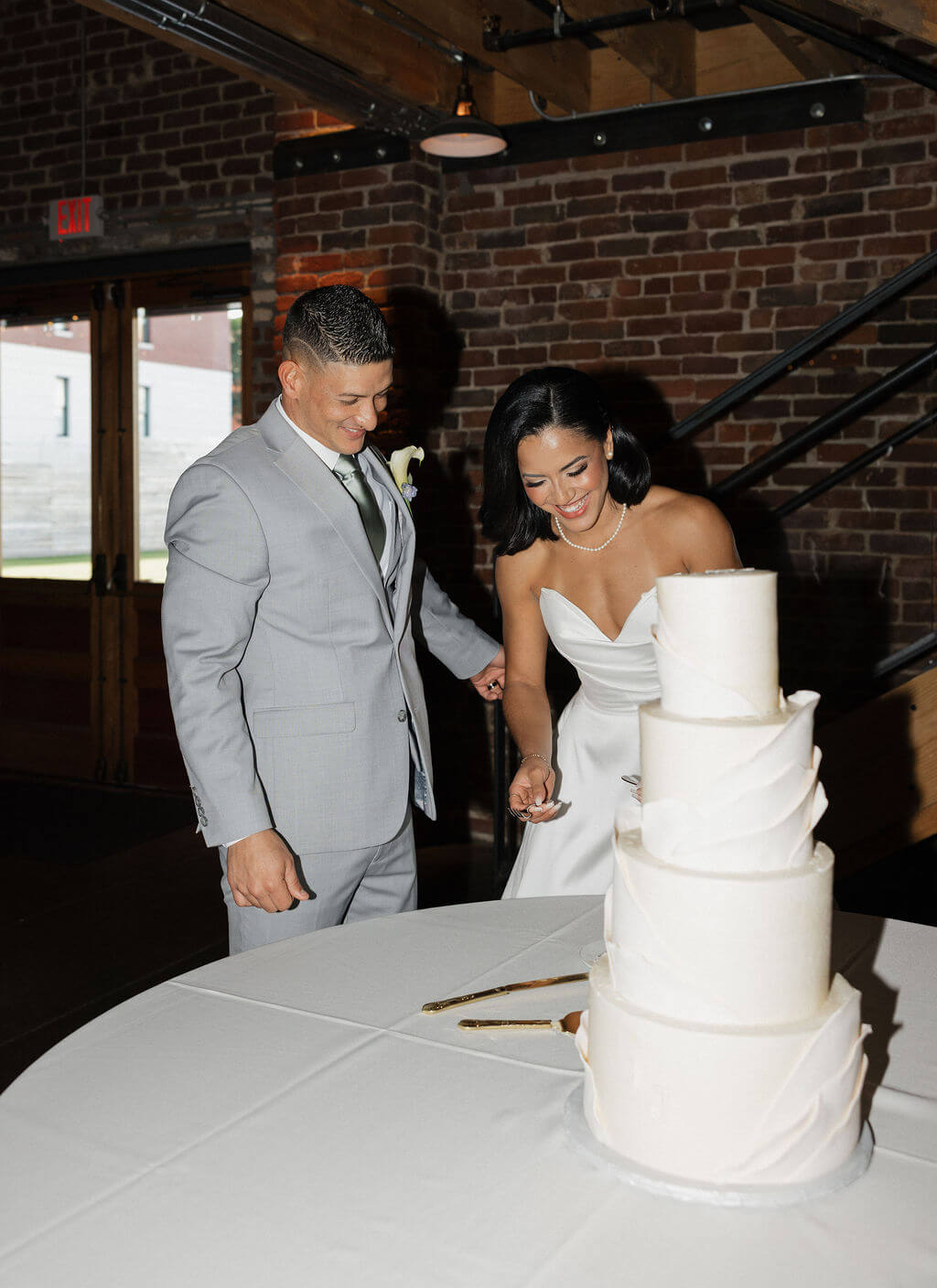 Bride and groom smiling as they cut their tiered white wedding cake inside The Mill and Mine.