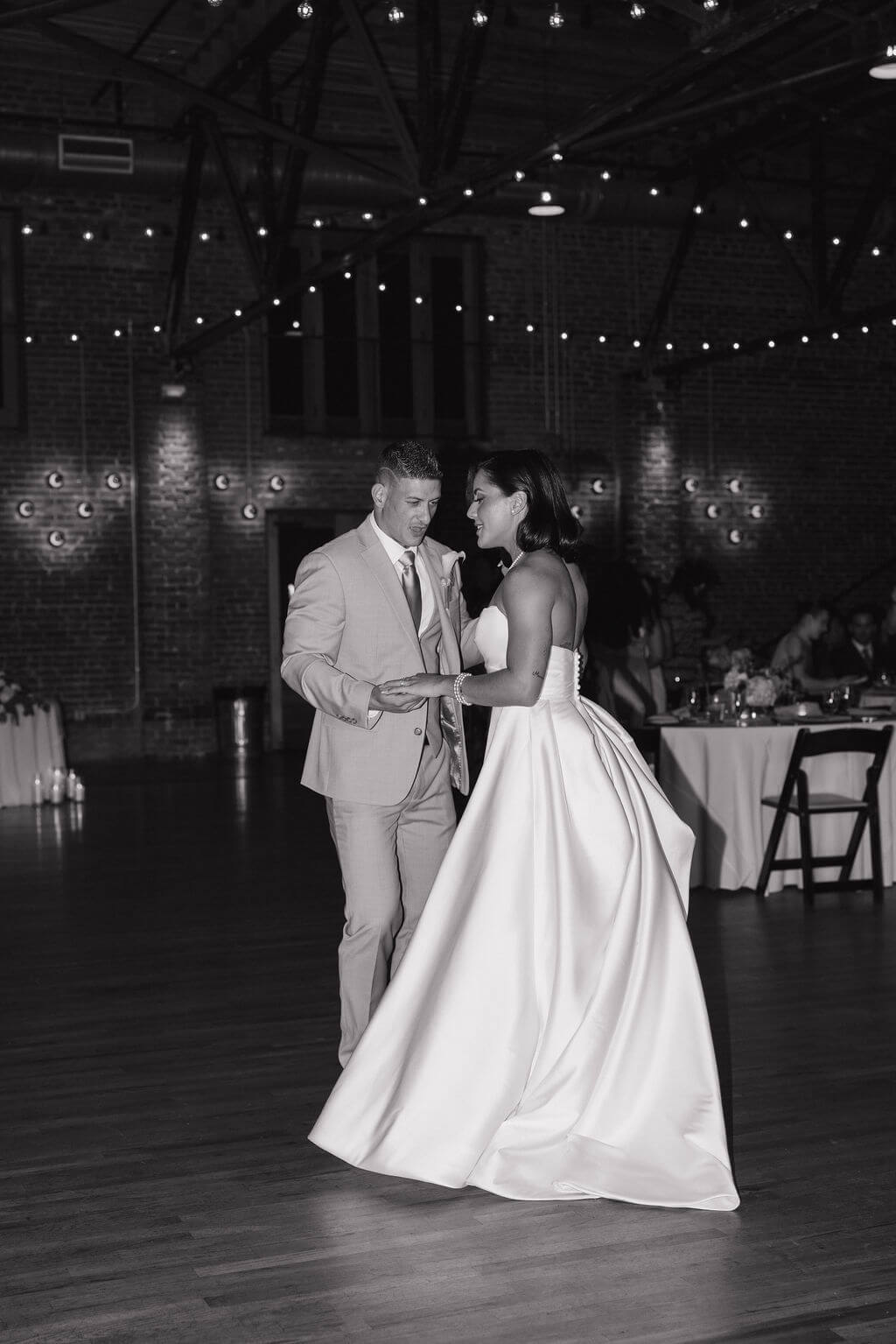 Black-and-white photo of the bride and groom slow dancing together during their wedding reception.