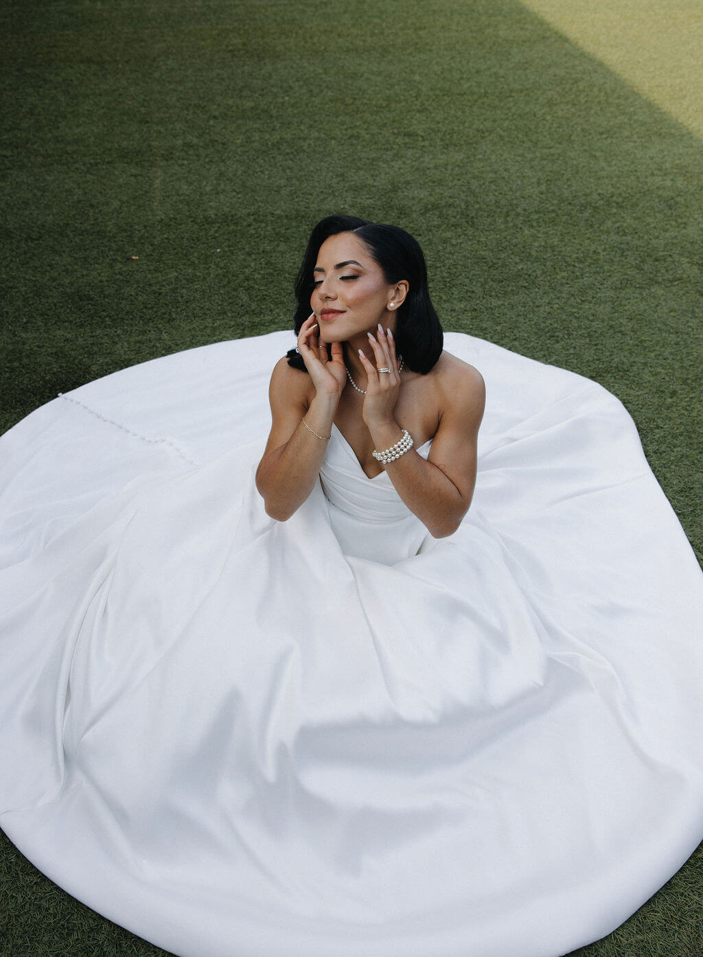 Overhead portrait of the bride sitting on the lawn surrounded by the full skirt of her white wedding gown.
