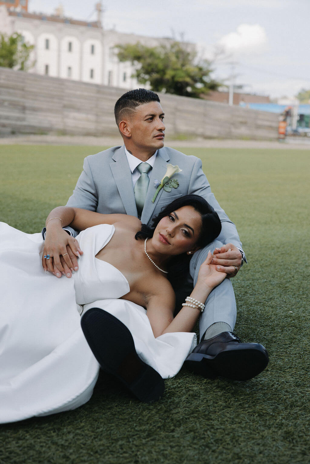 Bride reclining against the groom as they sit together on the grass during wedding portraits.