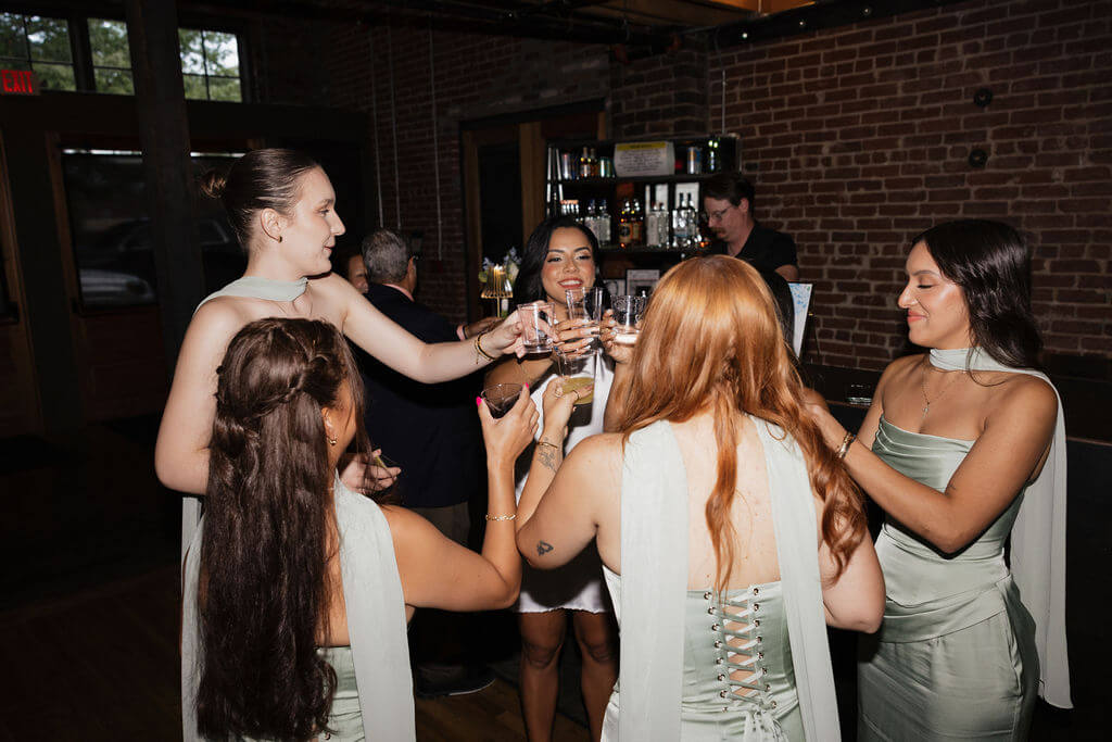 Bride and bridesmaids raising glasses for a celebratory toast beside the bar during the wedding reception.