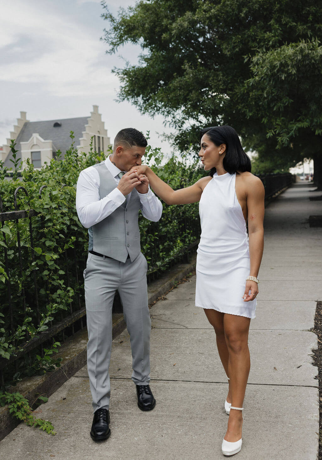 Groom kissing the bride’s hand as they walk together outside The Mill and Mine after she changed into a short white dress.