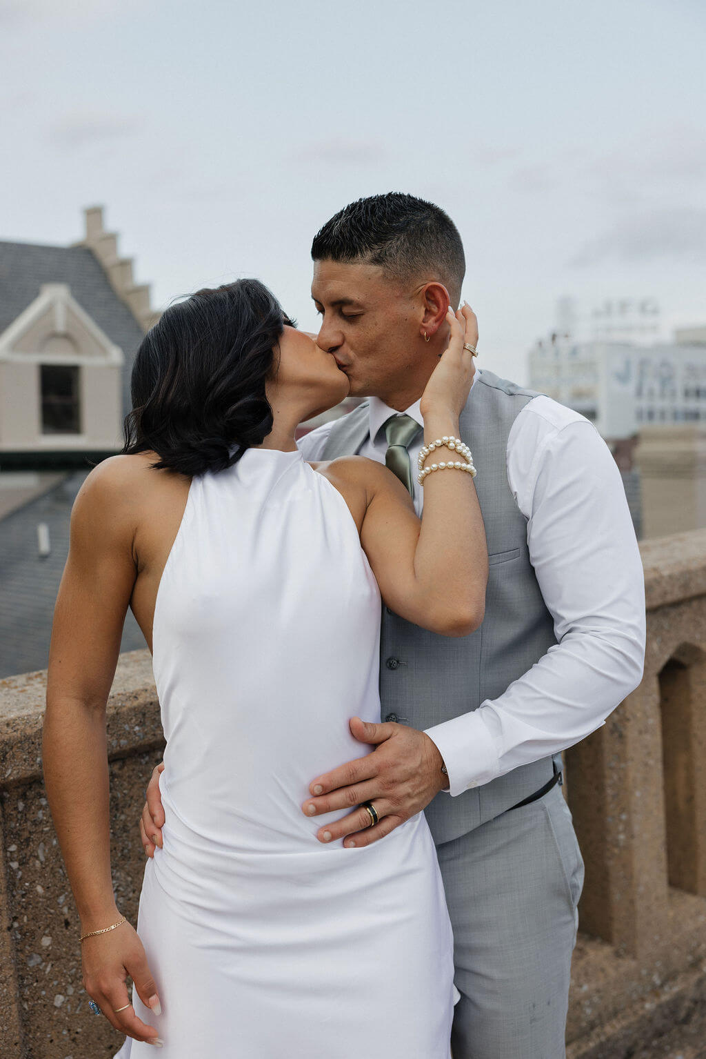 Bride in a short white dress kissing the groom beside a concrete railing during downtown Knoxville portraits.