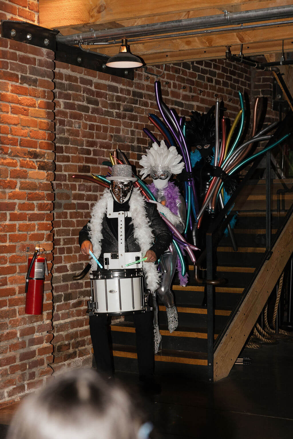 Costumed drummer entering the brick reception space during the couple’s lively Hora Loca celebration.