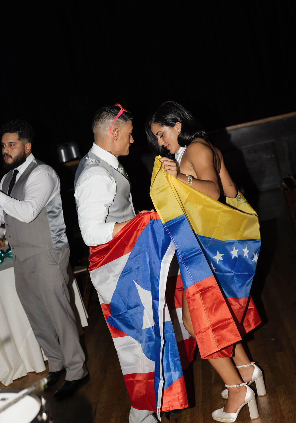 Bride and groom dancing together while wrapped in a colorful Venezuelan flag during the wedding reception.
