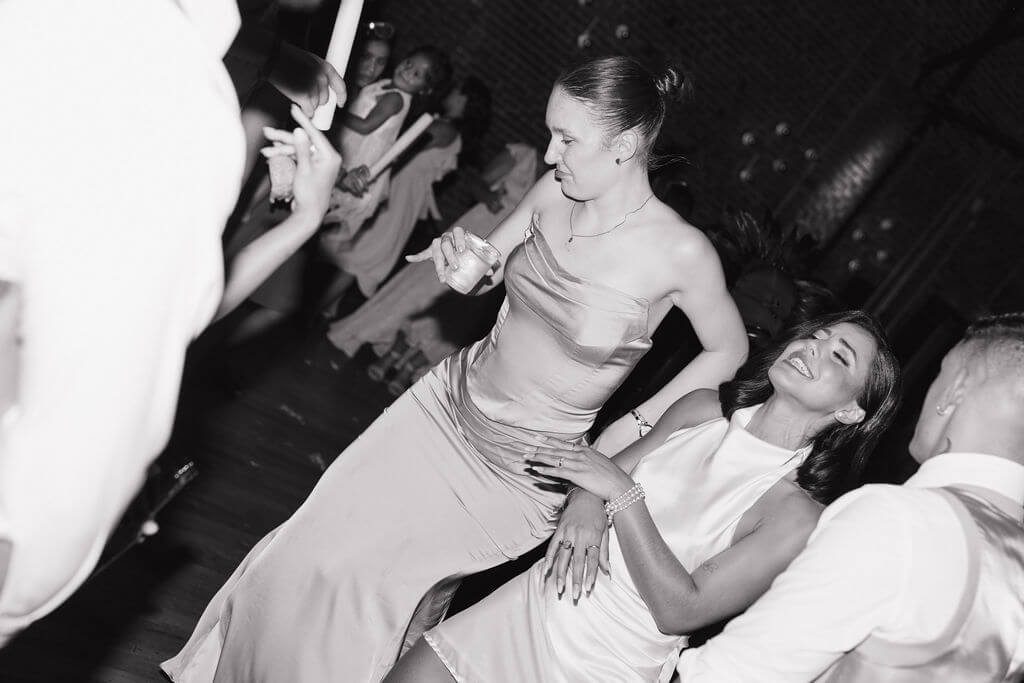 Black-and-white candid of the bride laughing and dancing with a wedding guest during the reception.