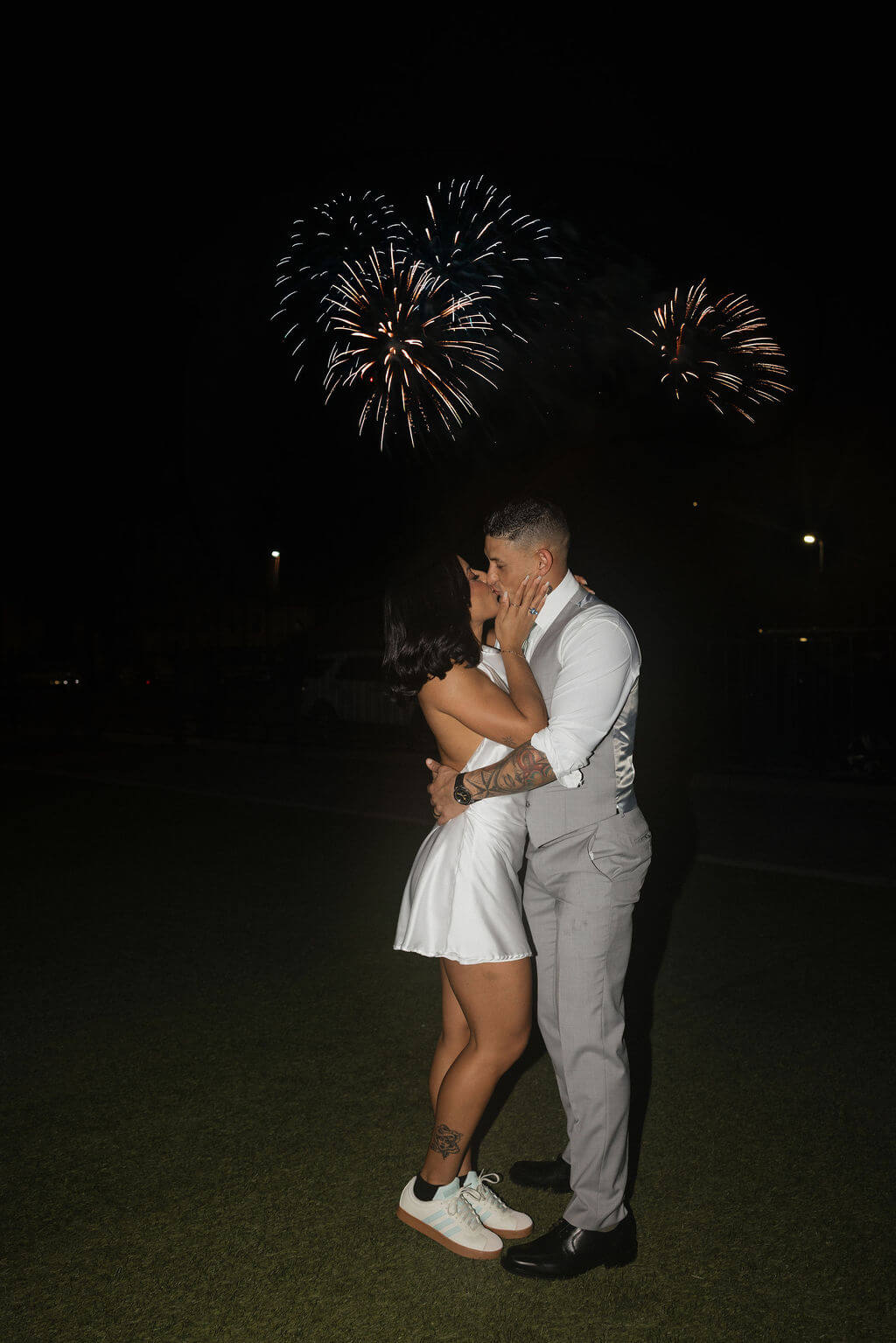 Bride and groom embracing outside at night as fireworks light up the sky behind them in downtown Knoxville.