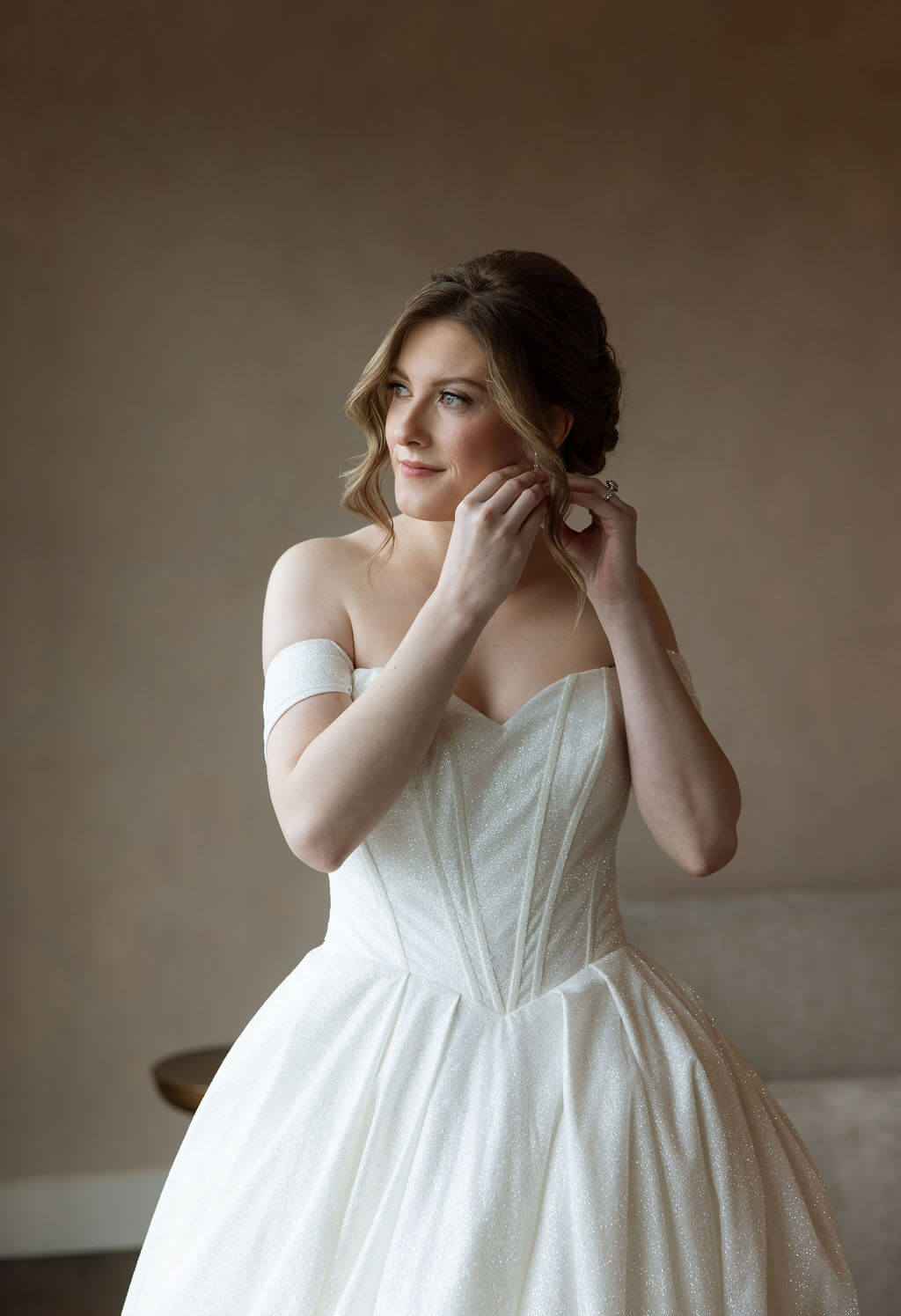 Bride adjusts her earring while getting ready in a strapless white wedding dress.