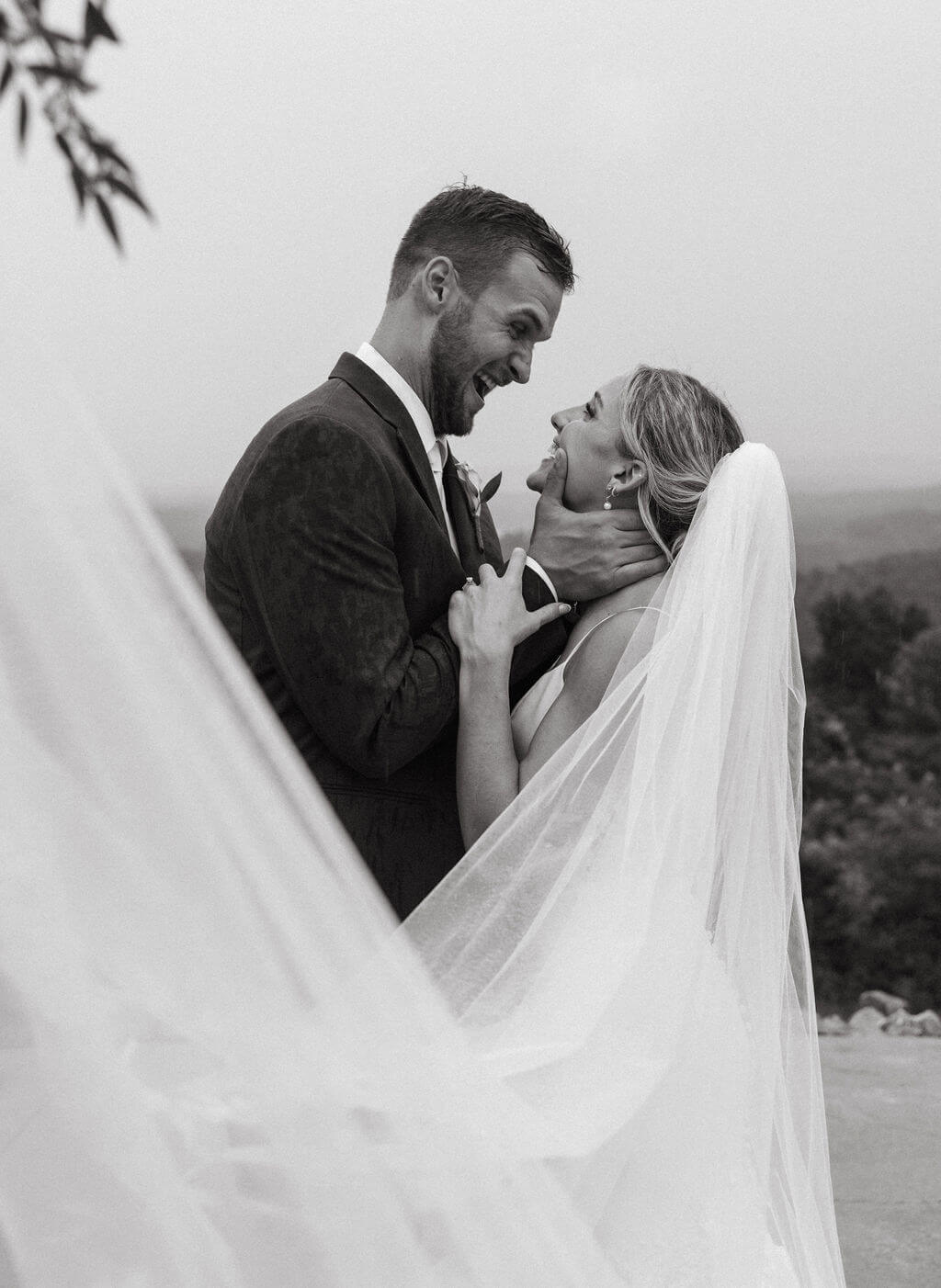Black-and-white close-up of a groom kissing the bride as her veil wraps around them.