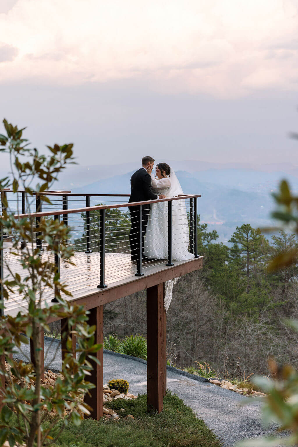 Bride and groom embrace on a wooden balcony overlooking the Smoky Mountains at sunset.