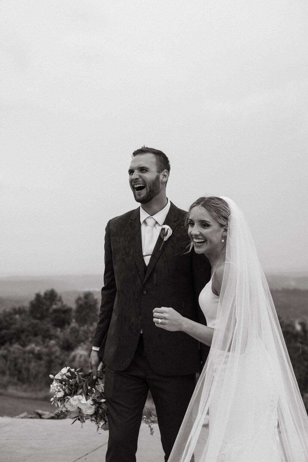 Black-and-white portrait of a smiling bride and groom standing together outdoors.