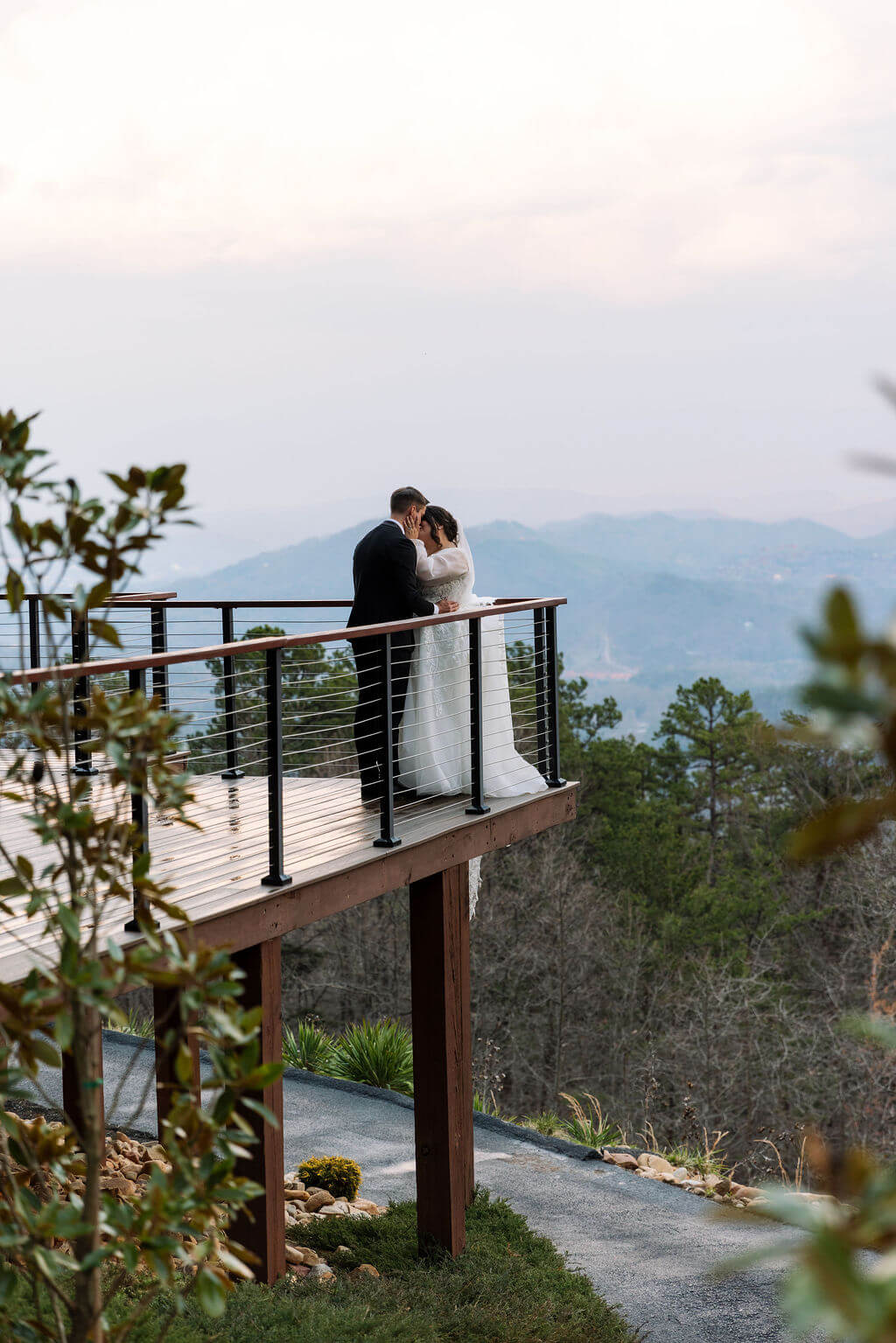 Bride and groom kiss on an elevated wooden balcony overlooking the Smoky Mountains.