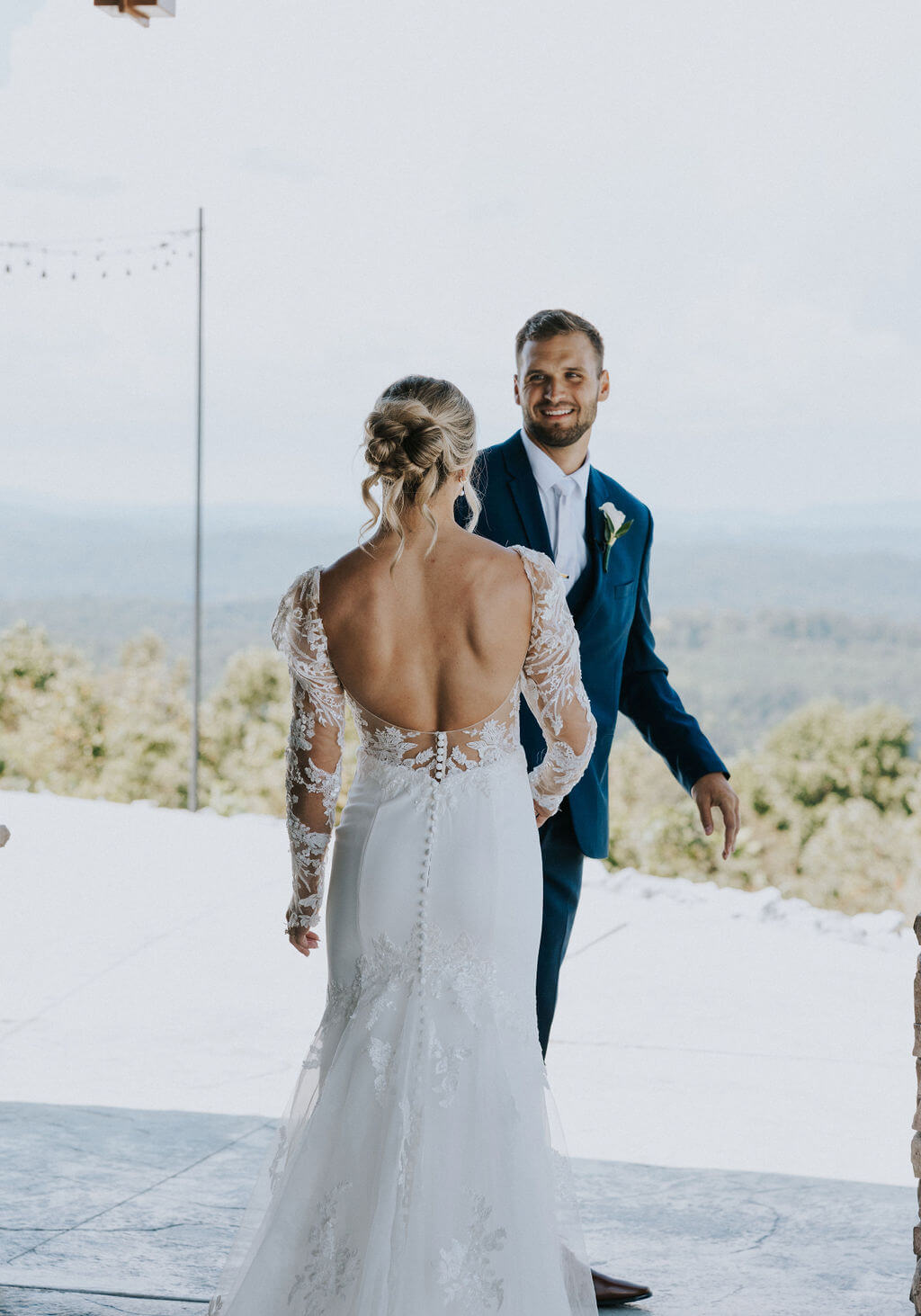 Groom smiles as he turns around to see the bride in her lace wedding dress.