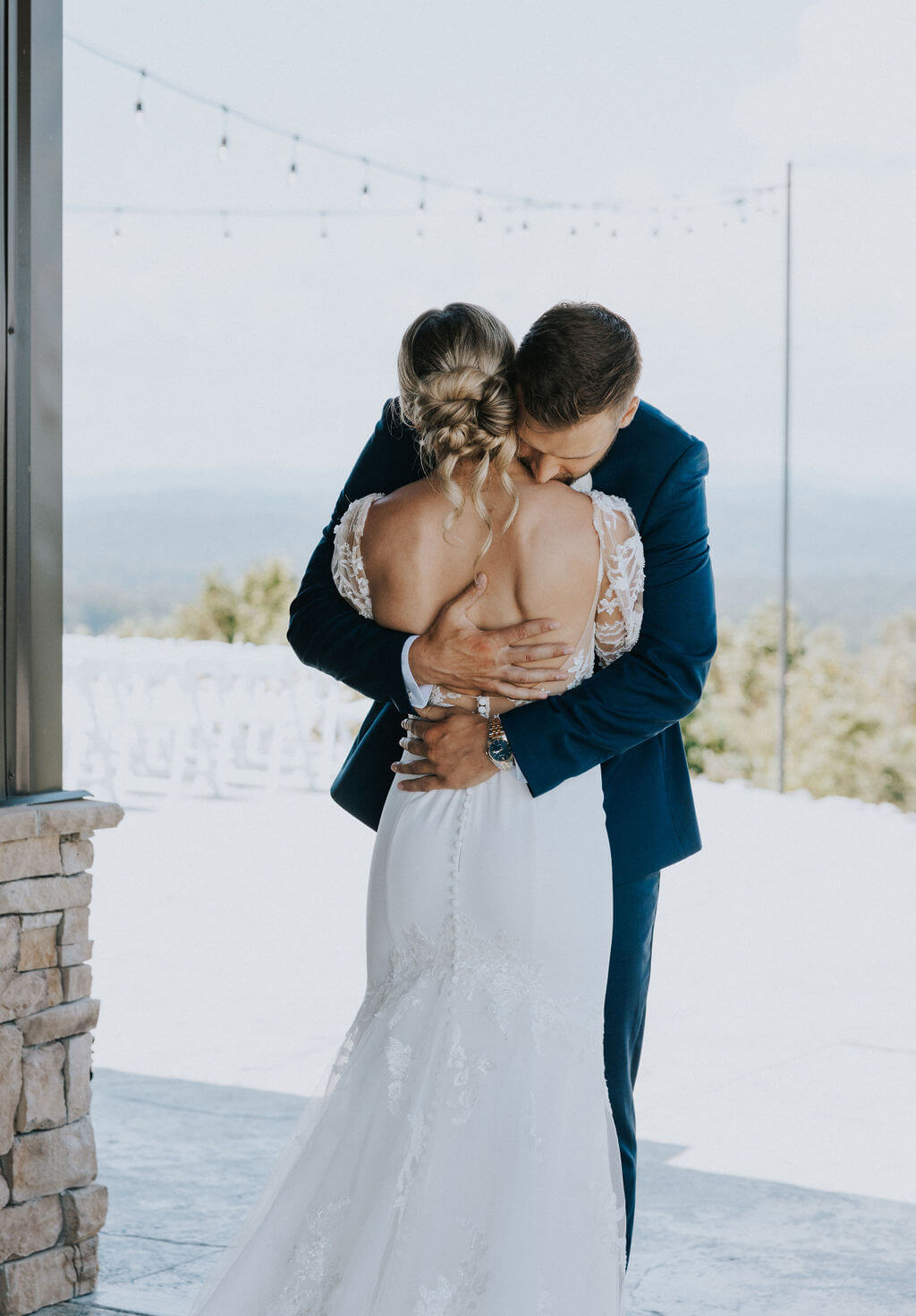 Groom embraces the bride during their first look beneath outdoor string lights.