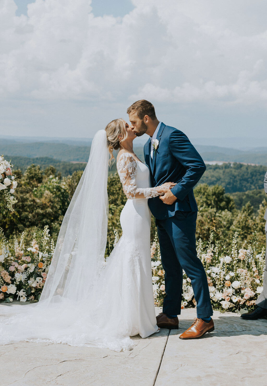 Bride and groom embrace on a mountain overlook surrounded by rolling green hills.