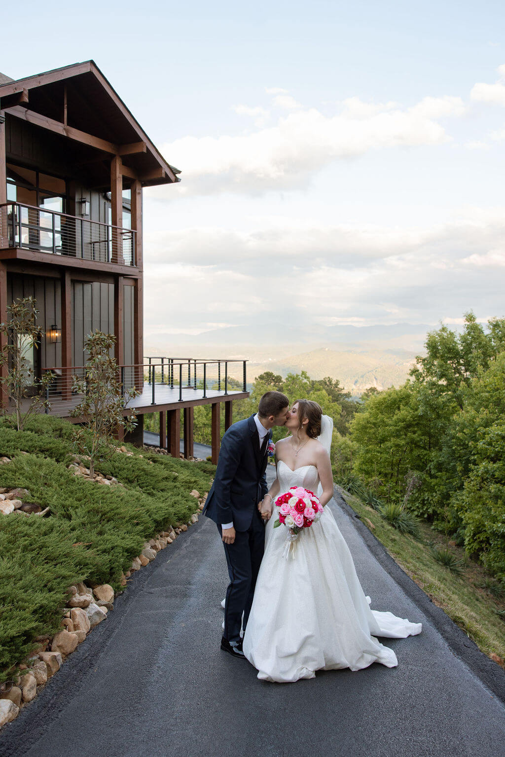 Bride and groom walk along a paved pathway outside a modern mountain wedding venue.
